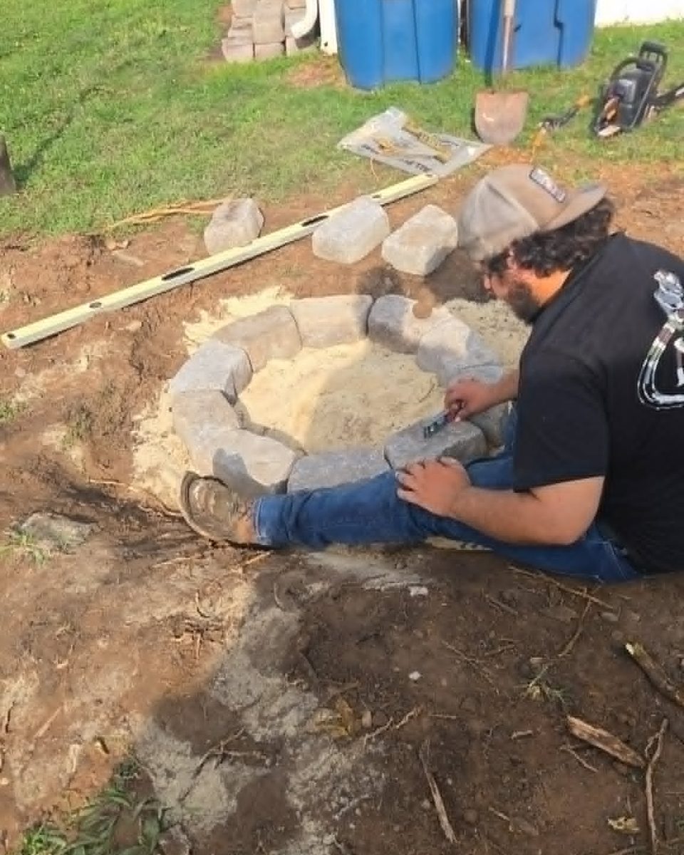 Stone fire pit ring being set block by block on a leveled bed at the center of a new gravel sitting area
