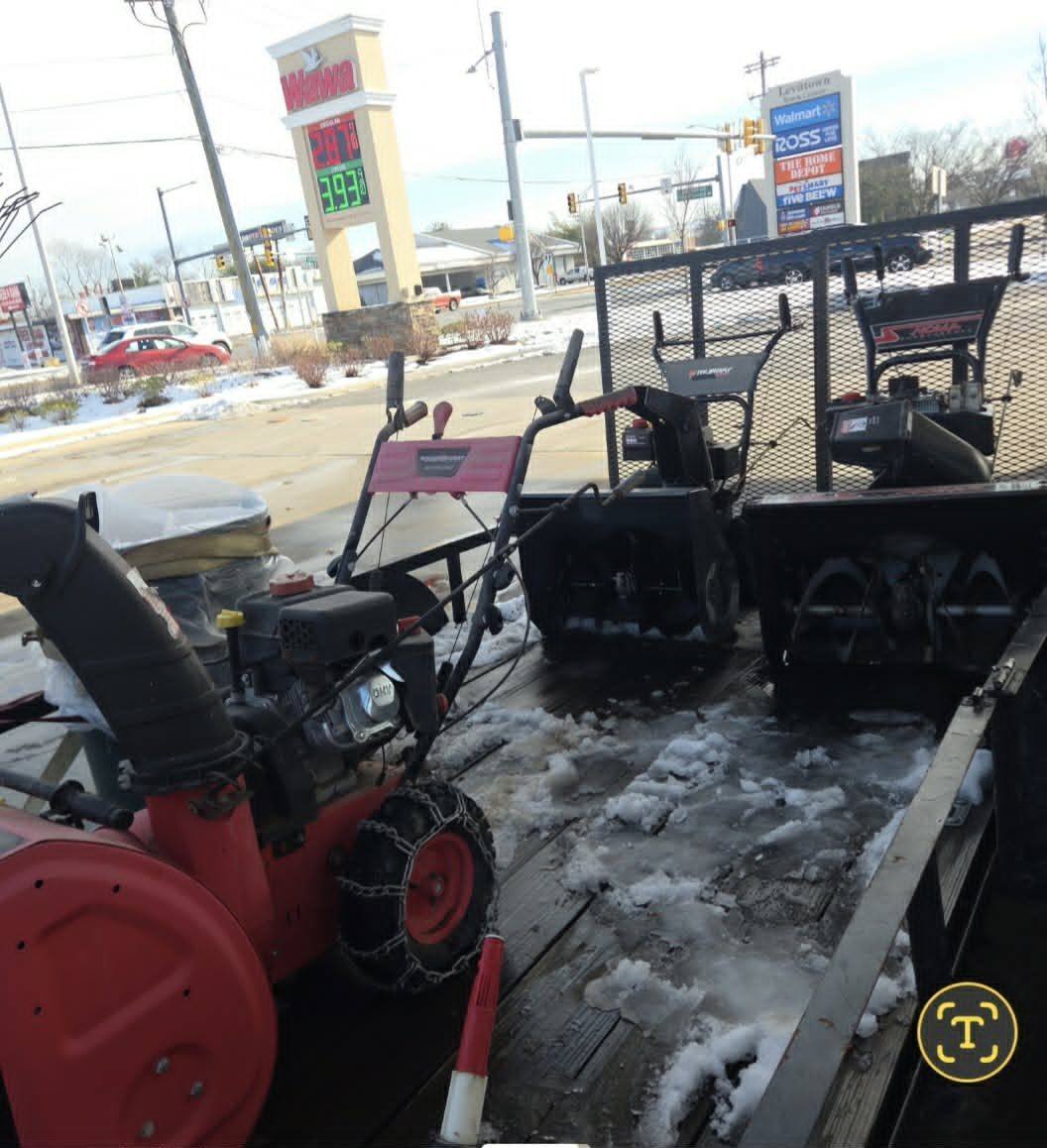 Three two-stage snow blowers with tire chains loaded on the trailer during a storm in Levittown