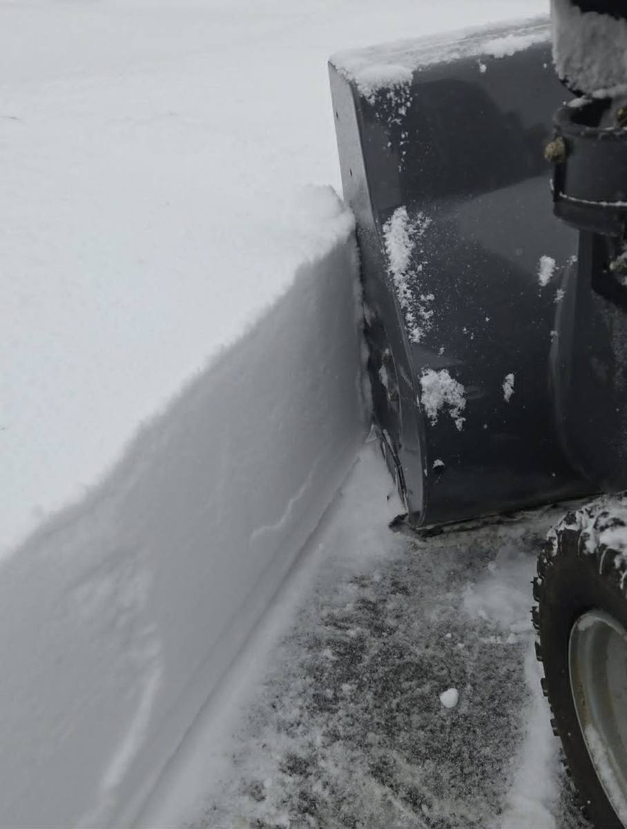 Two-stage snow blower cutting a clean vertical edge through deep snow down to the pavement